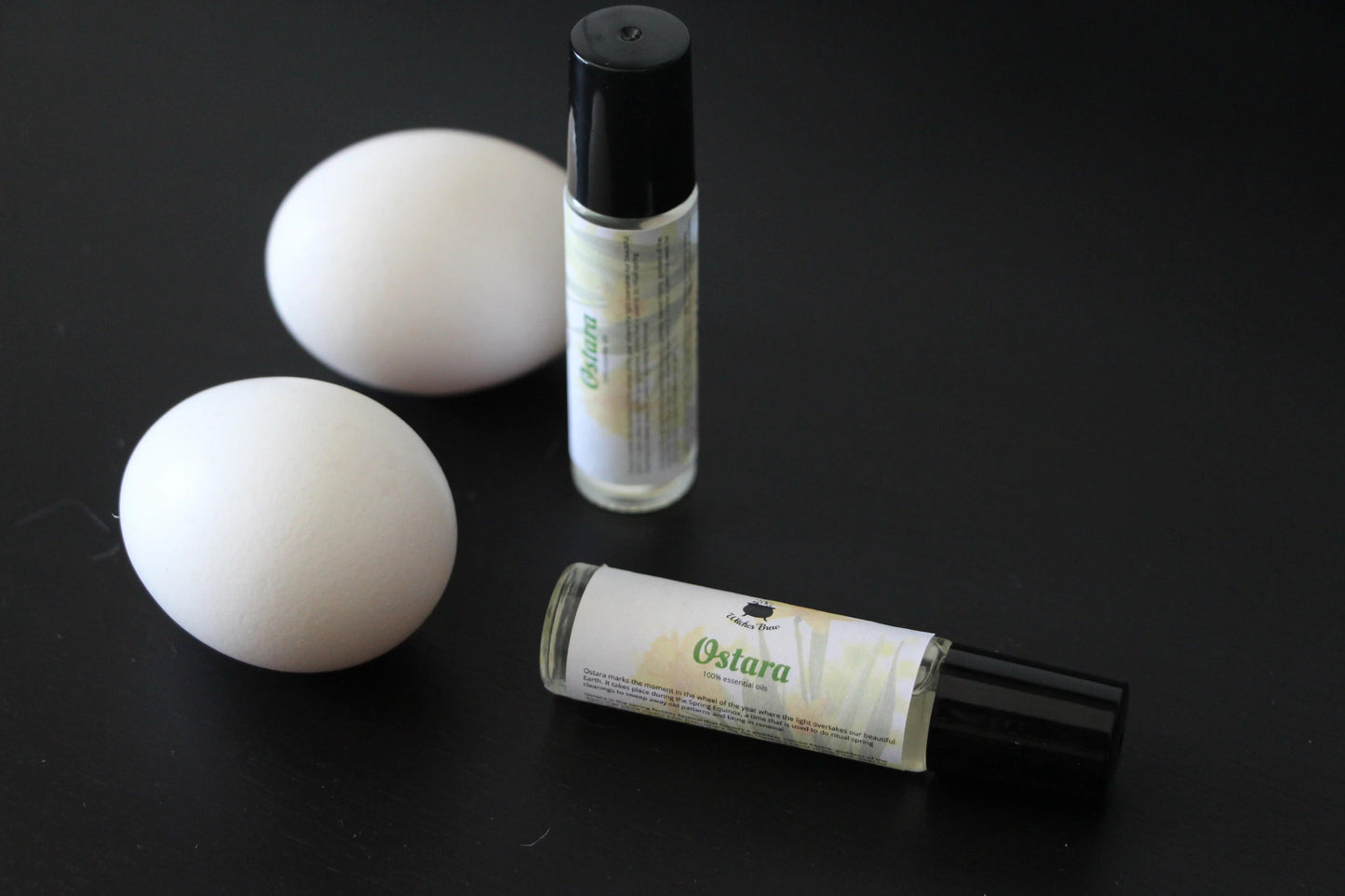 Ostara essential oil rollers and two white eggs on a black surface, Witches' Brew product
