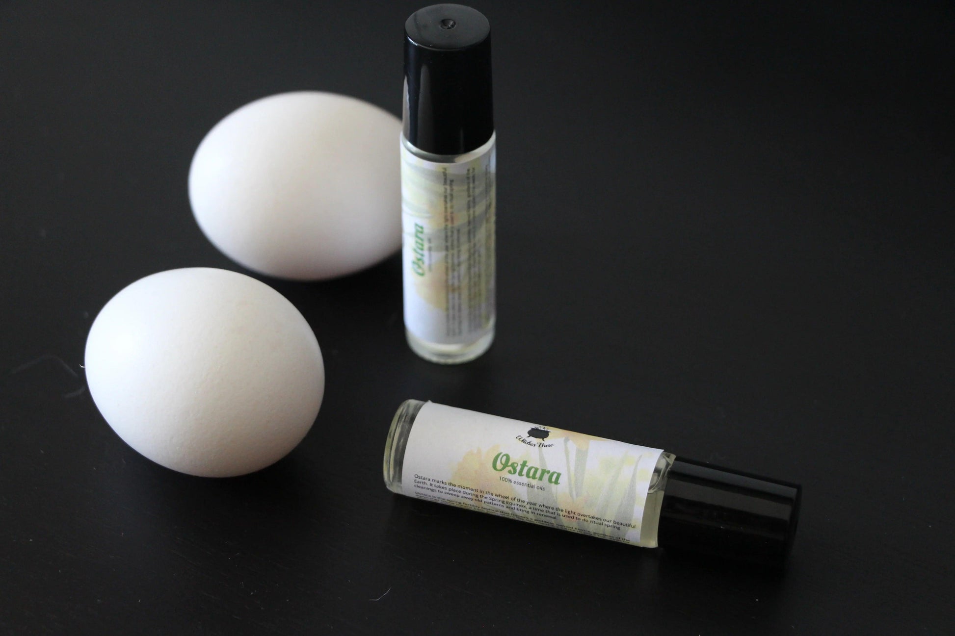Ostara essential oil rollers and two white eggs on a black surface, Witches' Brew product