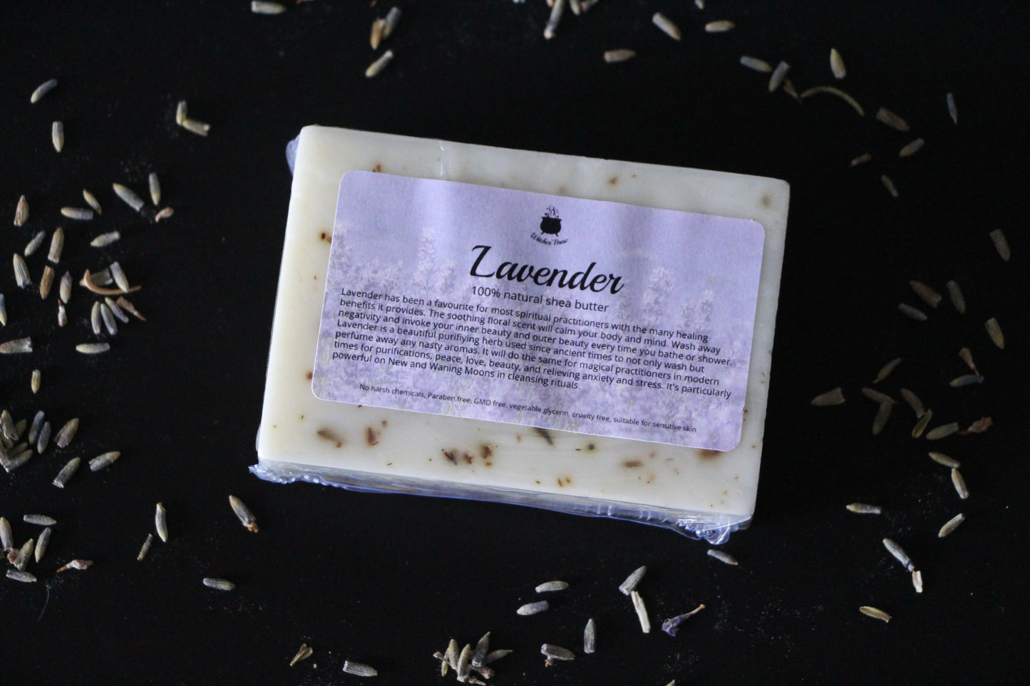 Lavender natural shea butter soap bar with label, surrounded by dried lavender buds on black surface