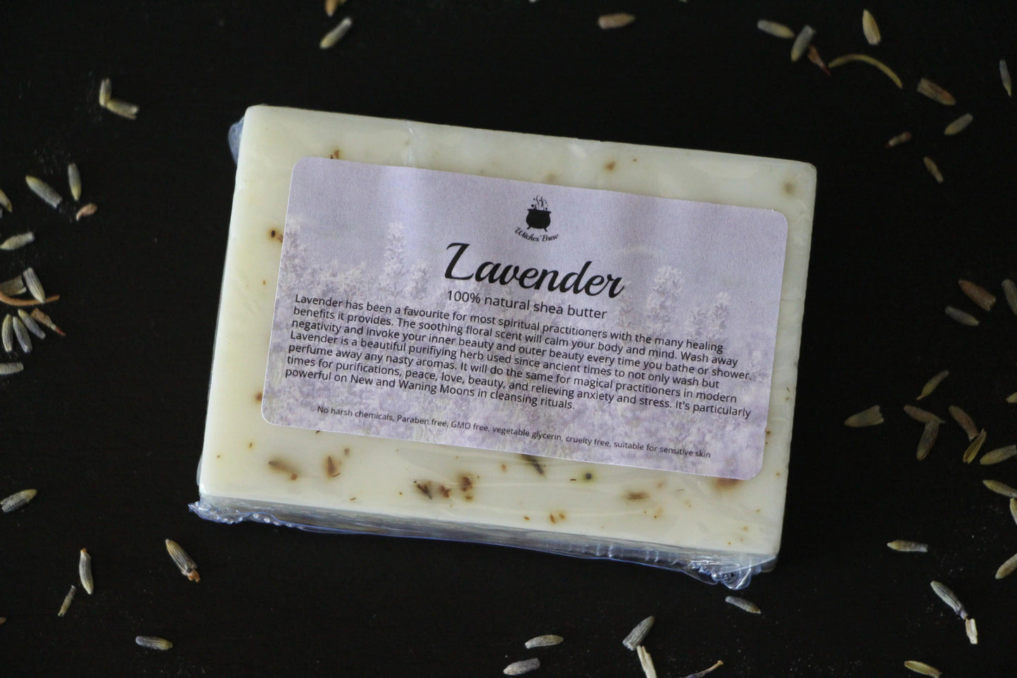 Lavender shea butter soap bar with label on black surface, surrounded by dried lavender buds