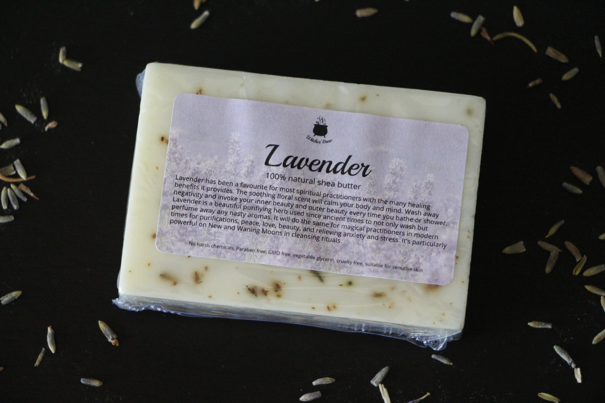 Lavender shea butter soap bar with label on black surface, surrounded by dried lavender buds