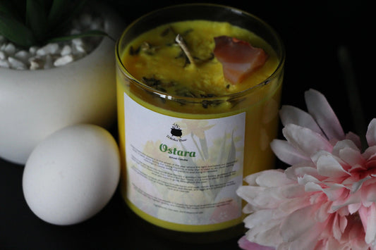 Ostara ritual candle with yellow wax, crystal, egg, succulent, and pink flower on black background