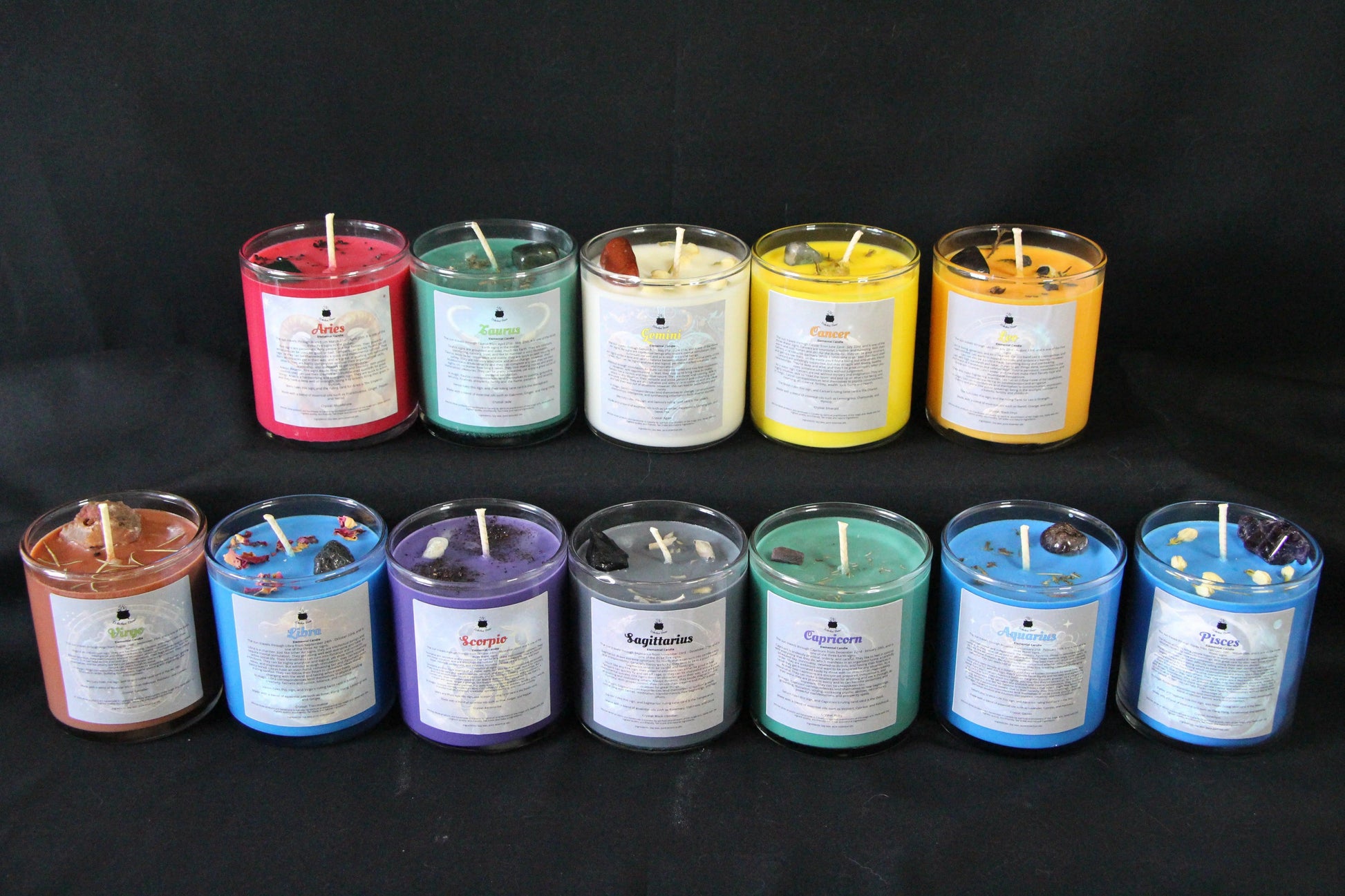 Hand-crafted zodiac crystal candles in colorful glass jars, arranged on a black background