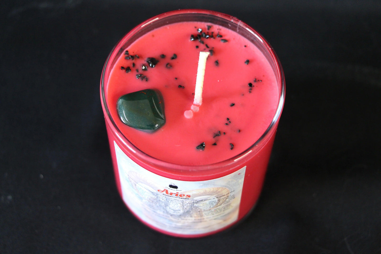 Red crystal candle with black herbs and green stone, sustainable hand-crafted for modern witch