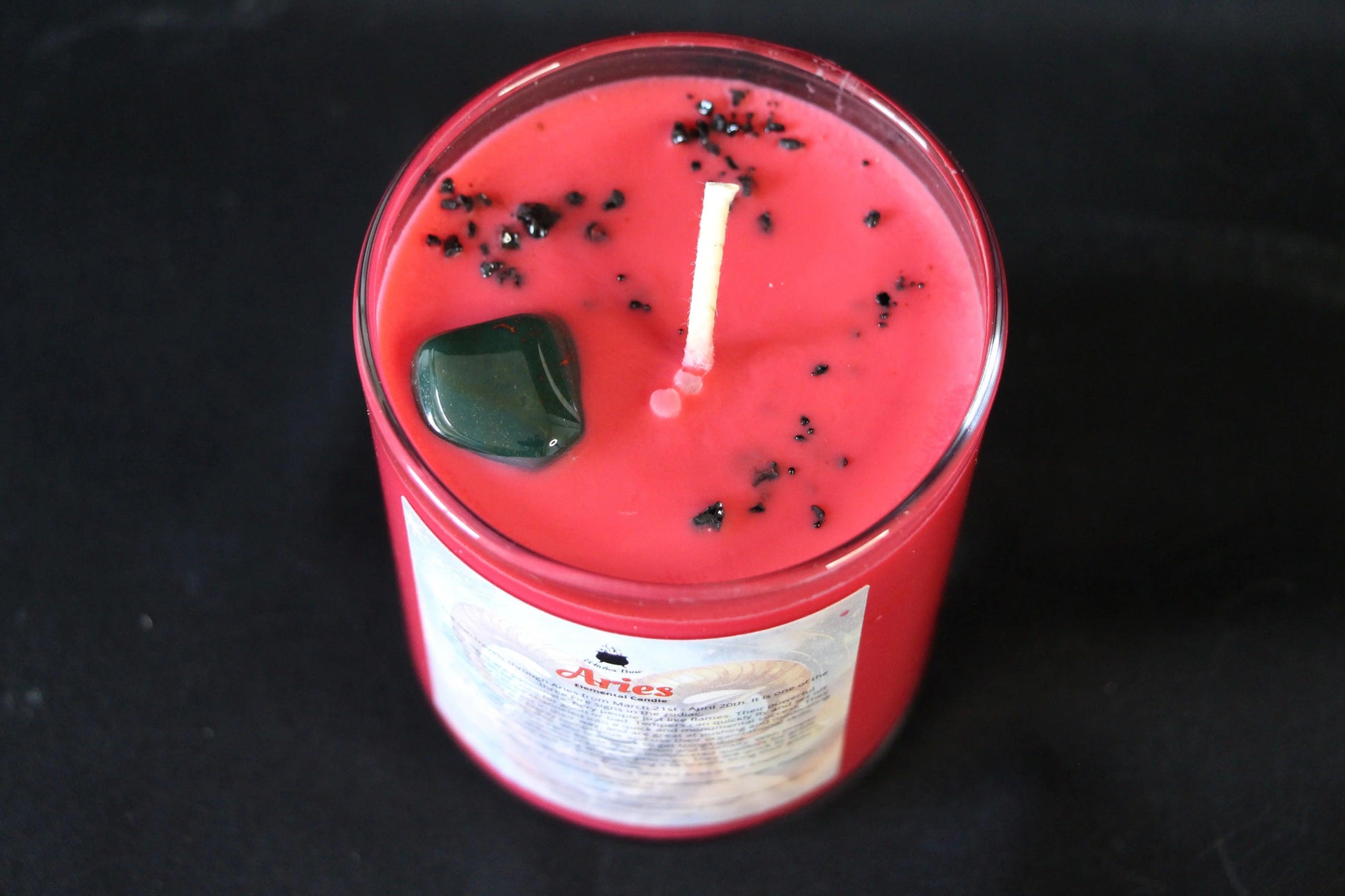 Red crystal candle with black herbs and green stone, sustainable hand-crafted for modern witch