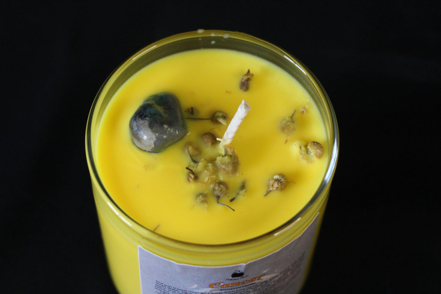 Yellow crystal candle with herbs and stone in glass jar on black background