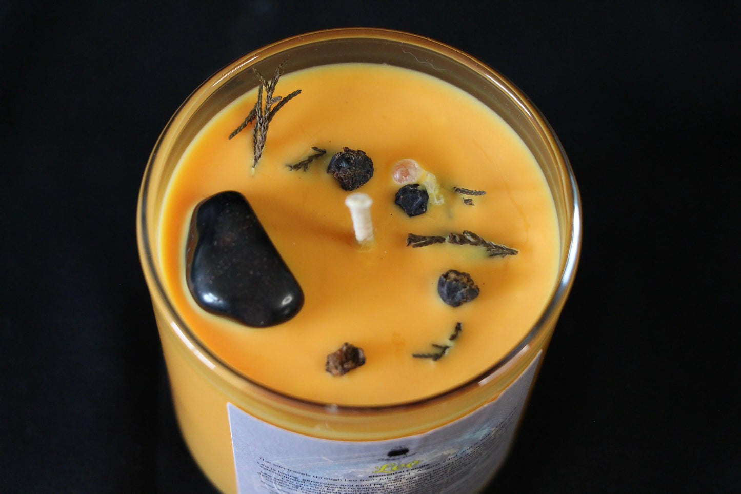 Handcrafted orange crystal candle with herbs and black stone for modern witch rituals