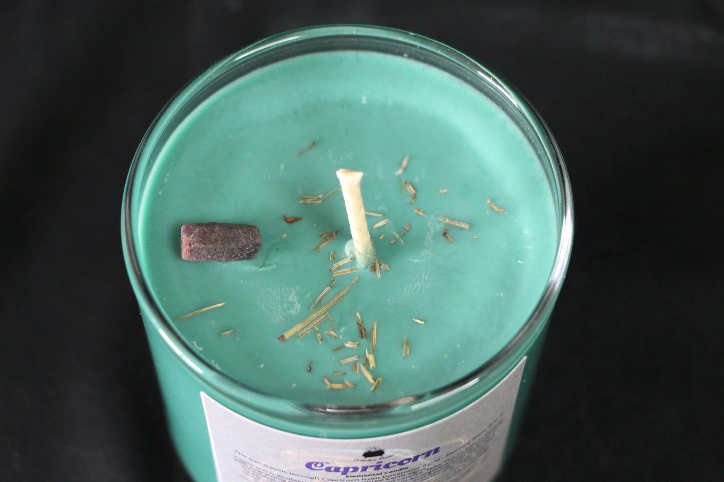 Green crystal candle with herb sprinkles in glass jar, sustainable witchcraft decor