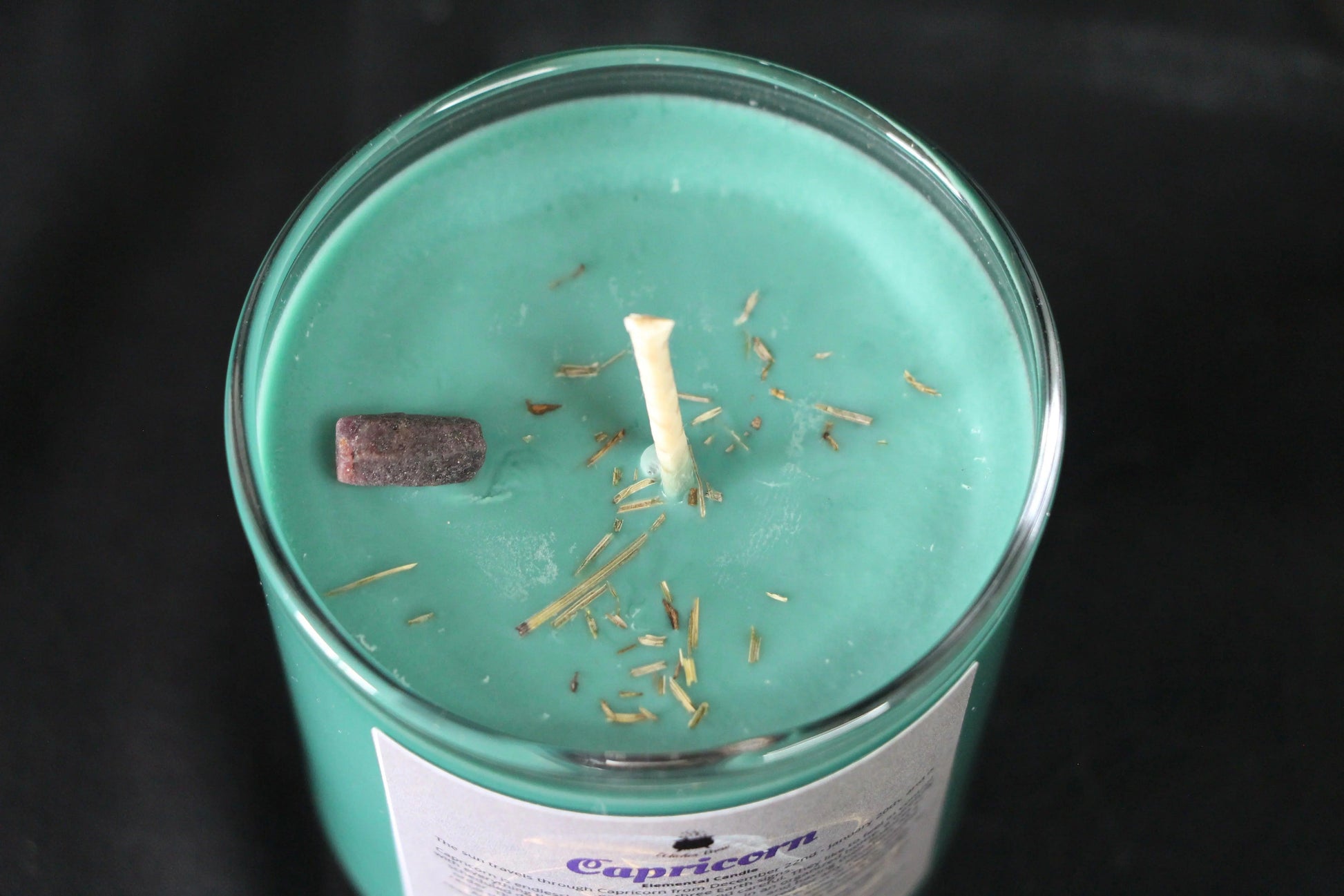 Green crystal candle with herb sprinkles in glass jar, sustainable witchcraft decor