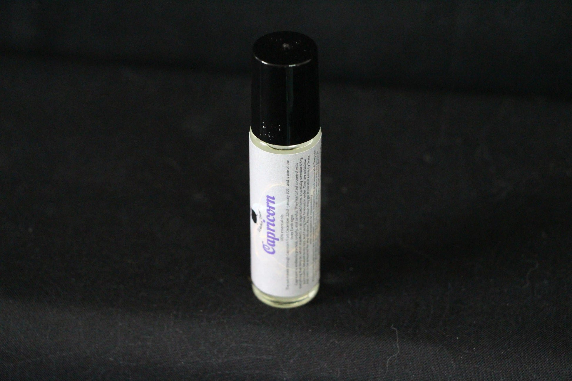 Capricorn essential oil roll-on bottle with black cap on a dark background