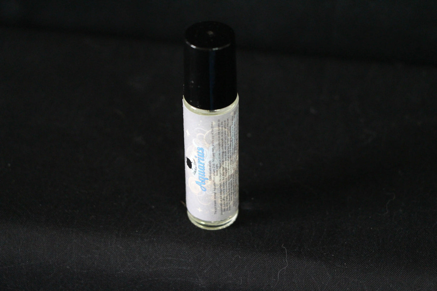Aquarius essential oil roll-on bottle on black background, modern witch ritual tool