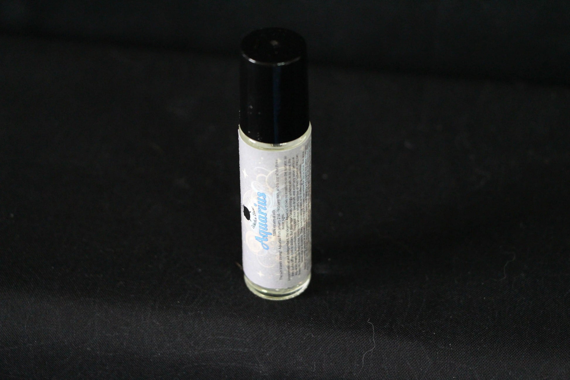 Aquarius essential oil roll-on bottle on black background, modern witch ritual tool