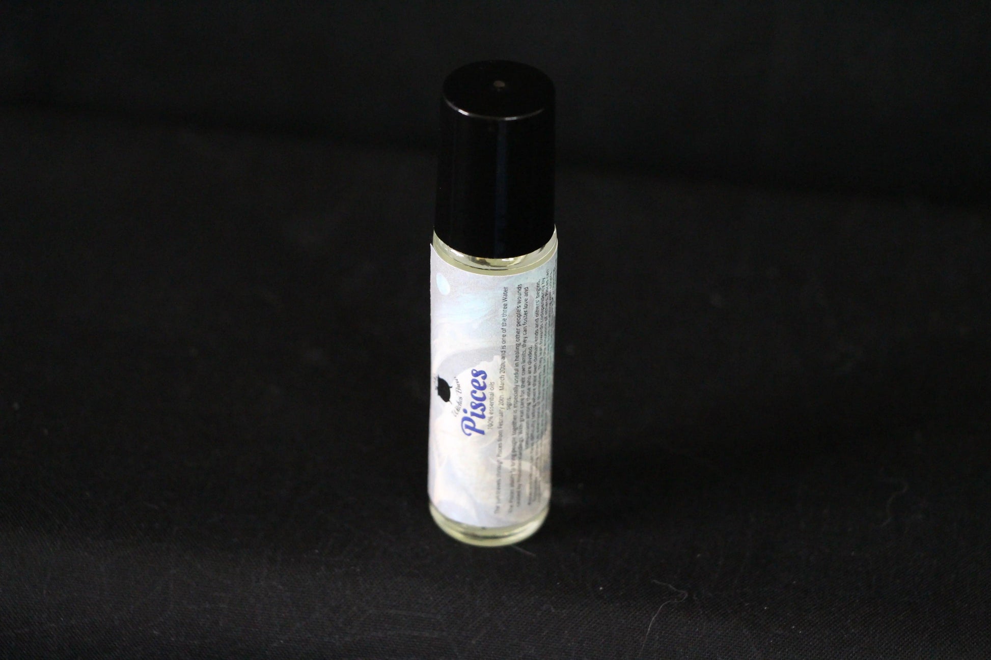 Pisces essential oil roll-on bottle on black background, sustainable witch ritual tool
