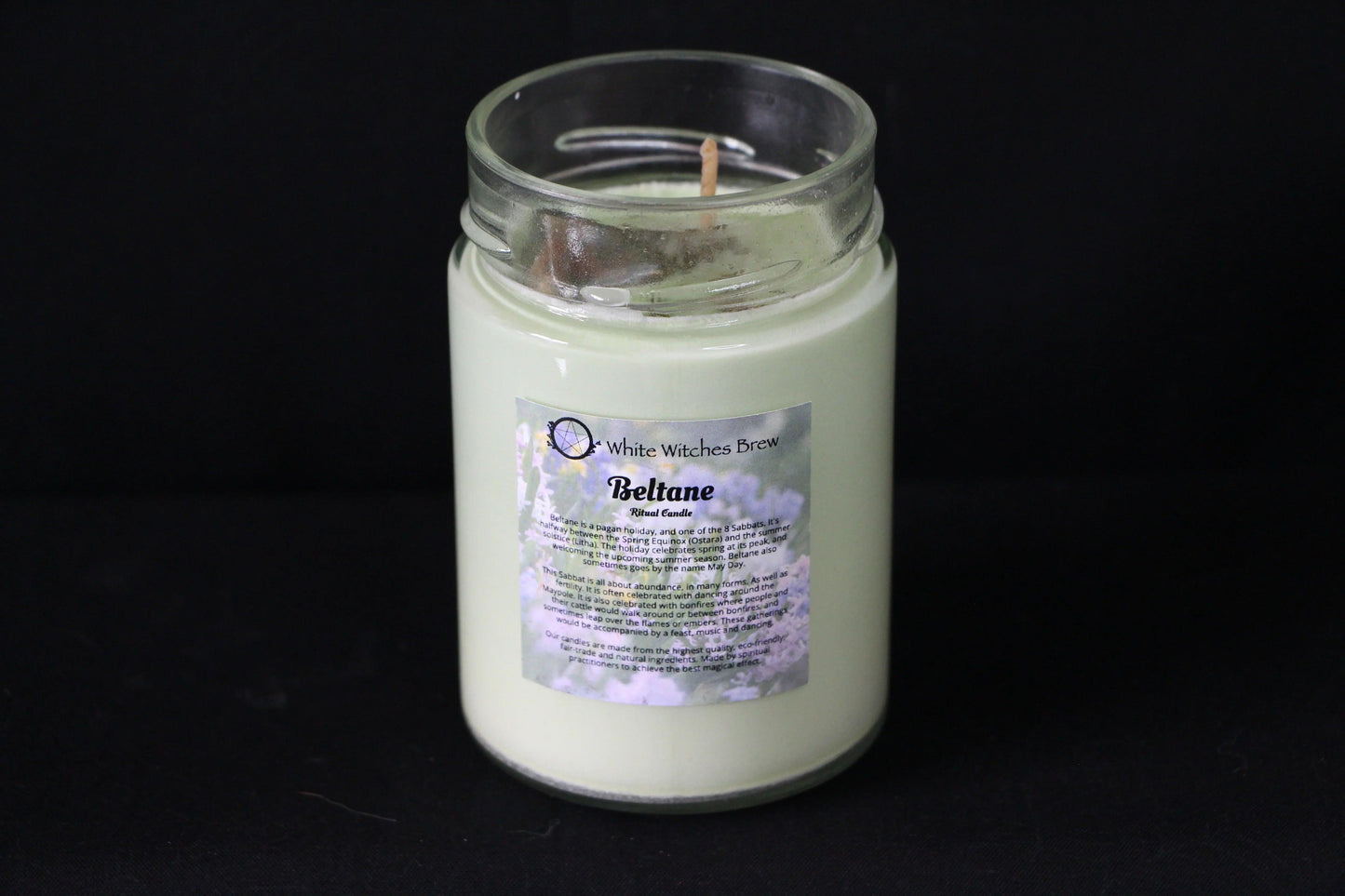 Handcrafted Beltane ritual candle in glass jar with floral label on black background