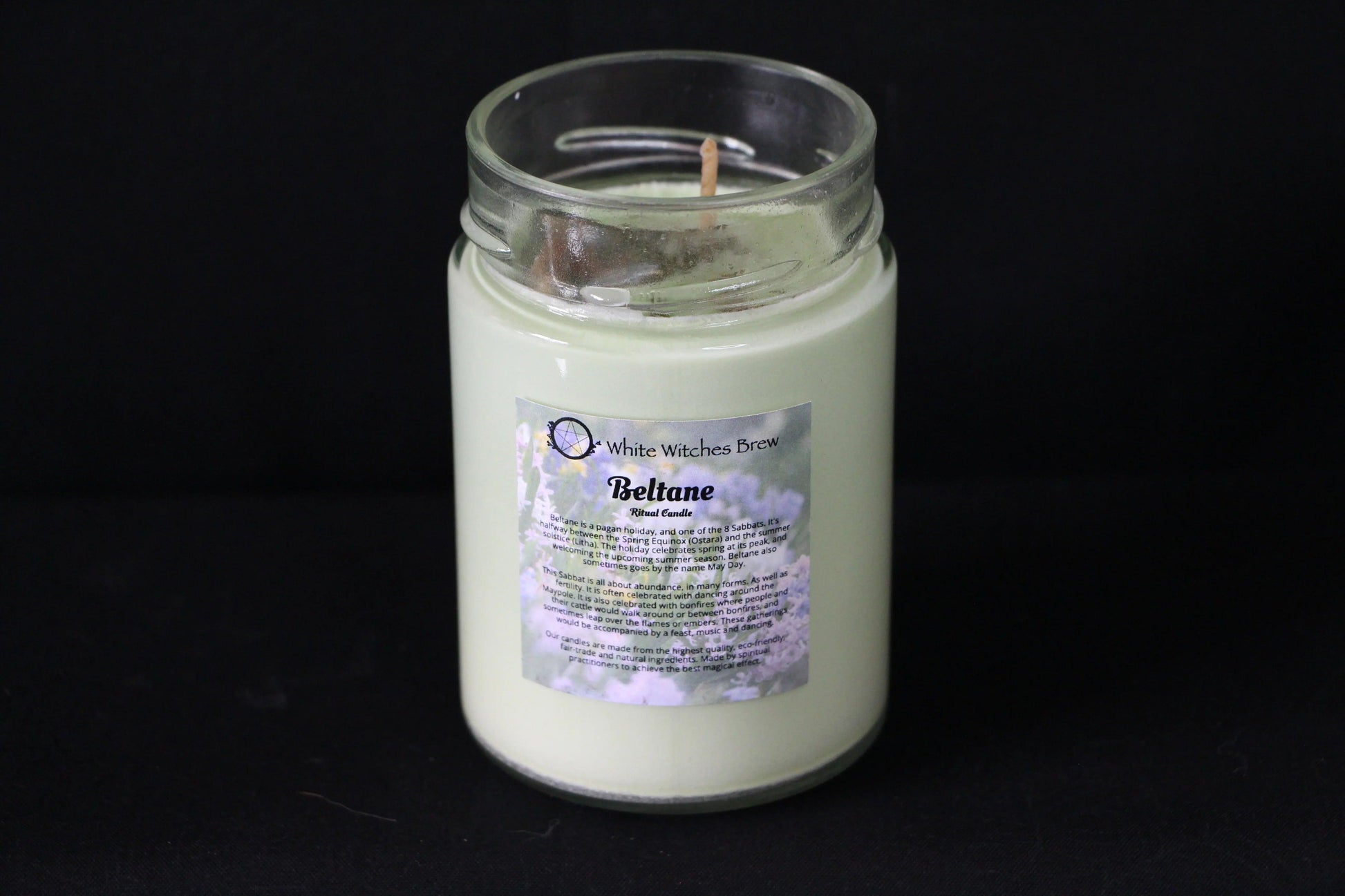Handcrafted Beltane ritual candle in glass jar with floral label on black background