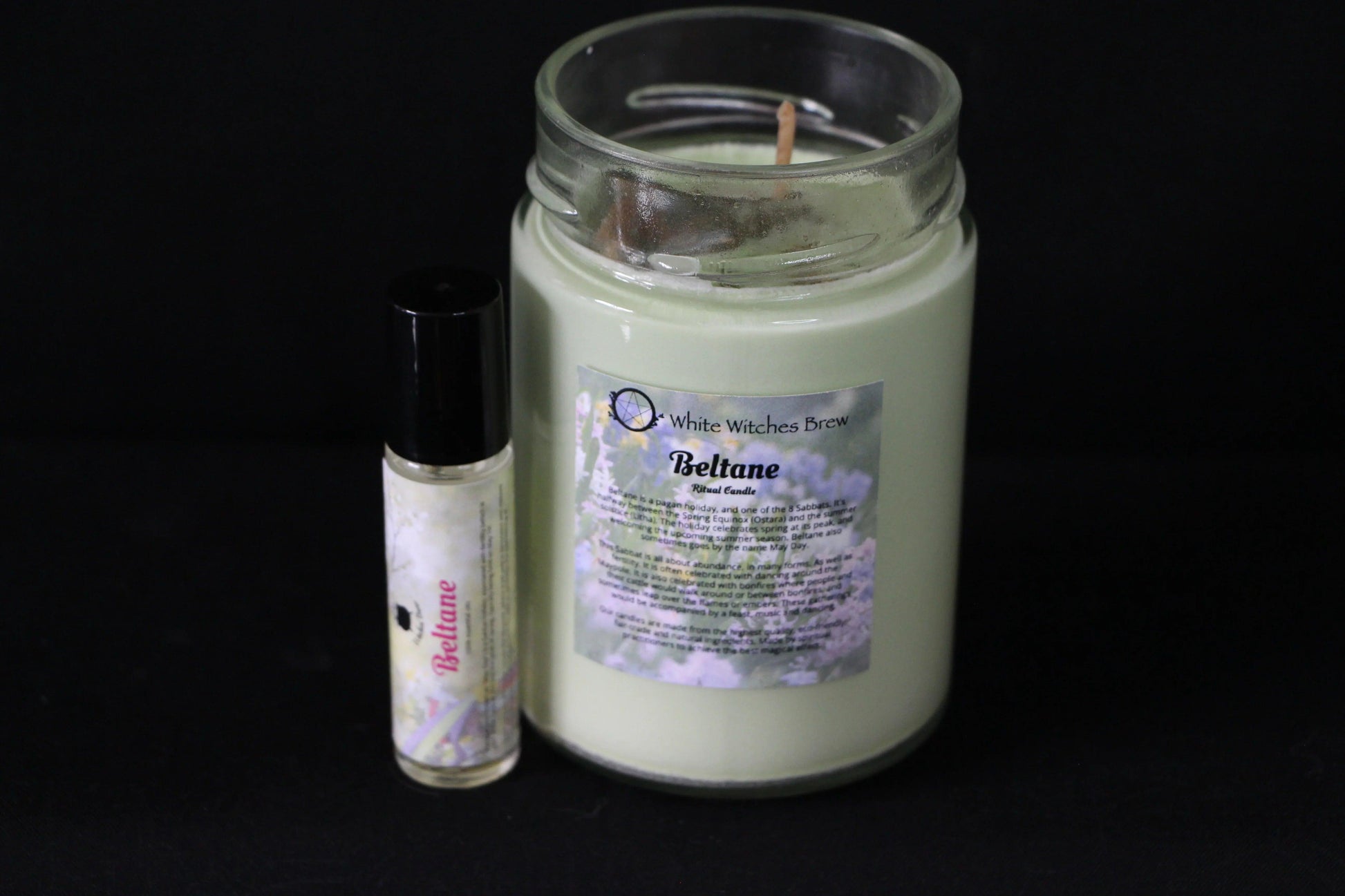 Beltane ritual candle and essential oil with floral label on black background