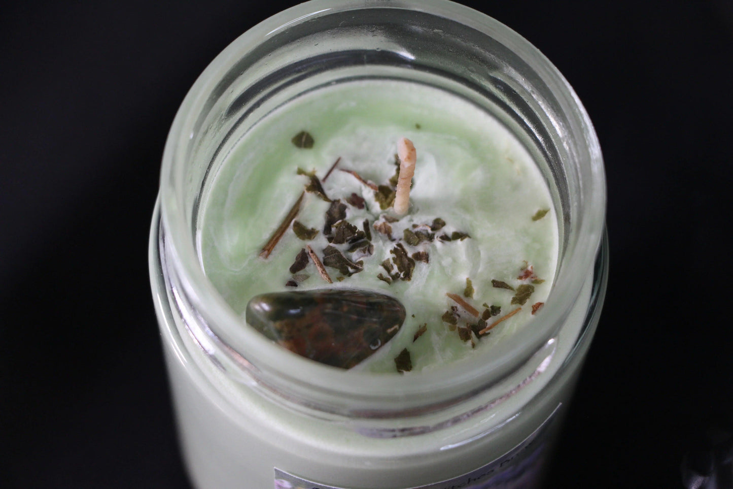 Green crystal candle in glass jar with herbs and gemstone on top, ritual decor