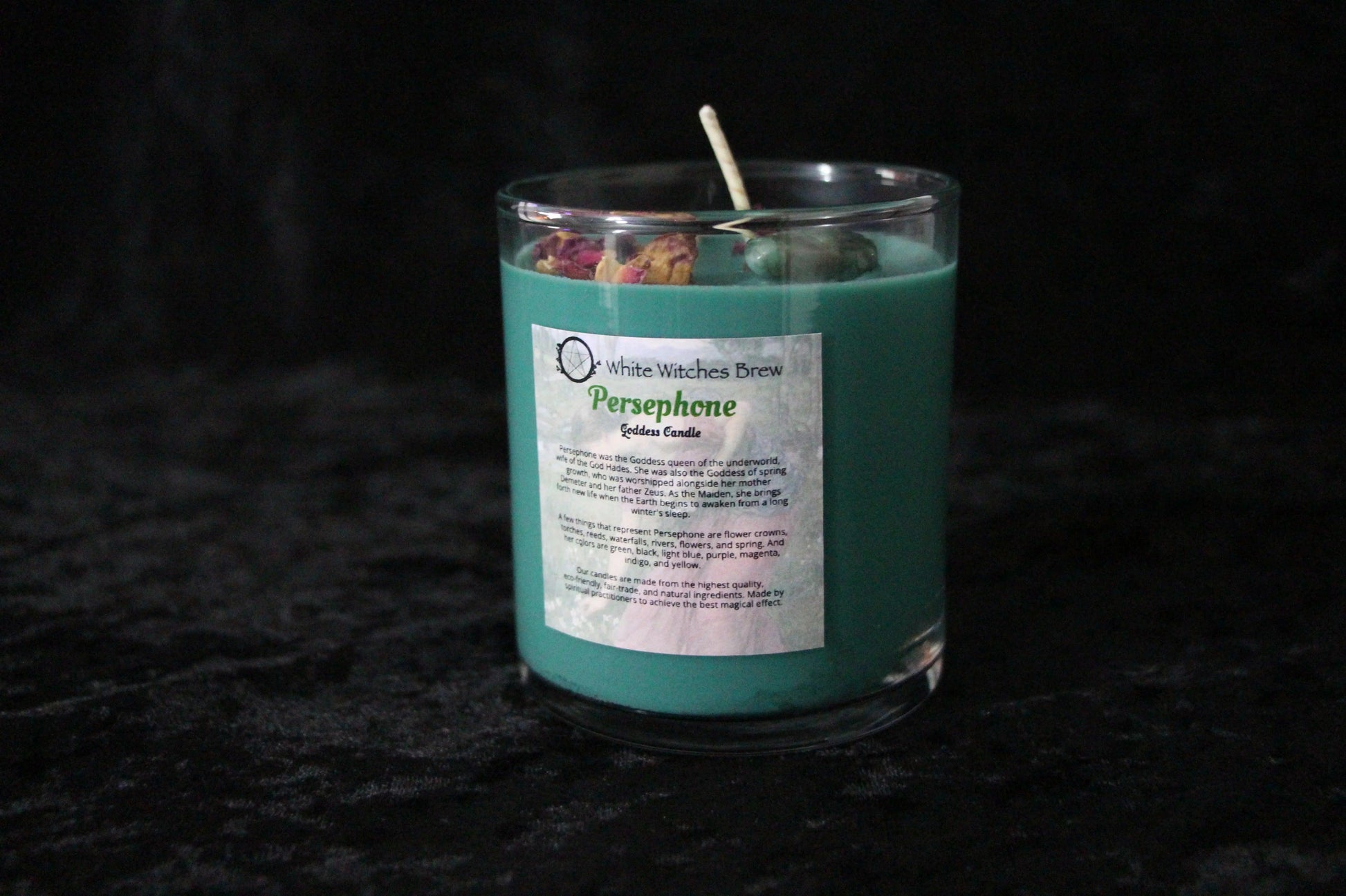 Hand-crafted teal crystal candle labeled Persephone by Witches' Brew on black velvet