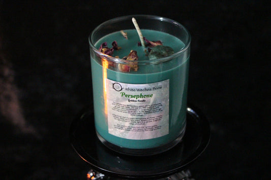Hand-crafted turquoise candle labeled Persephone with dried botanicals, on black background