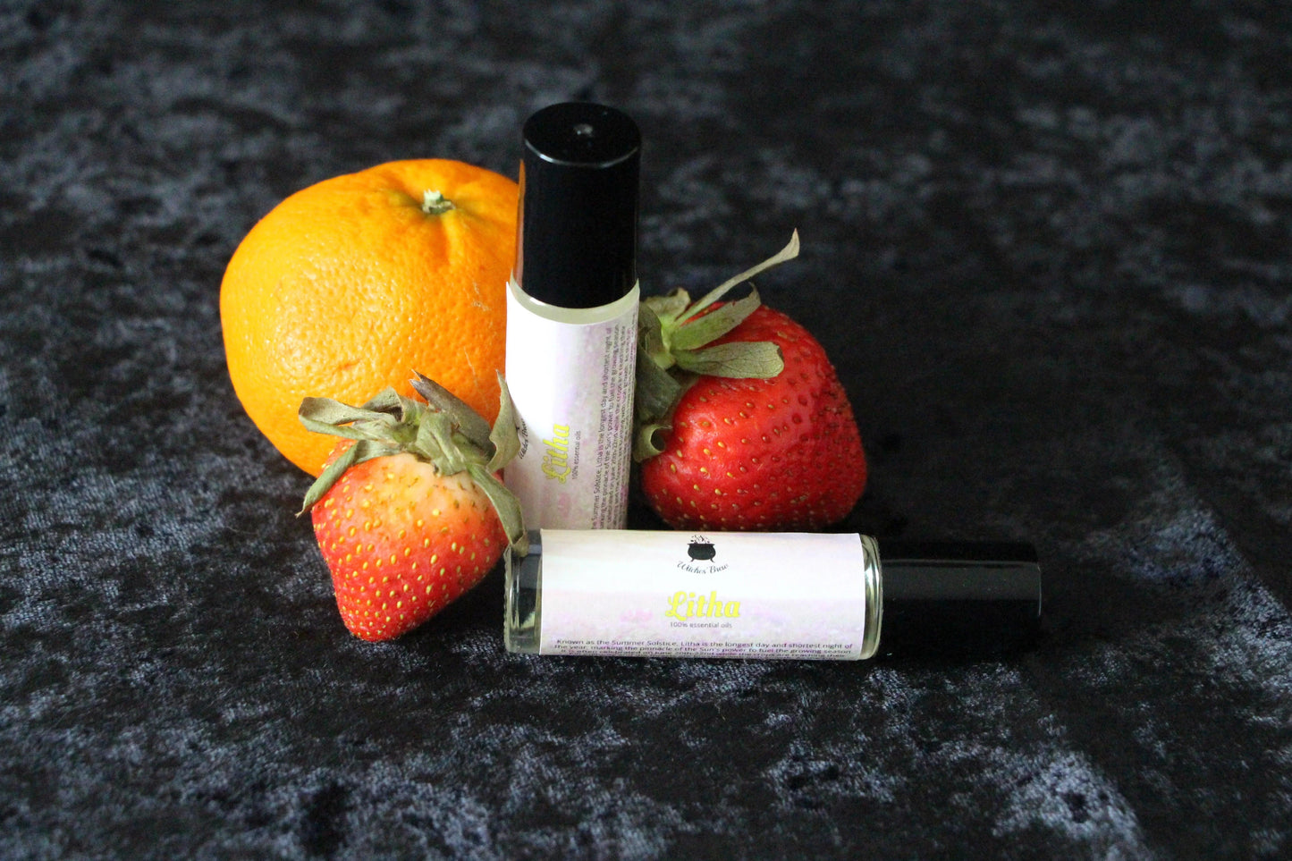 Hand-crafted Litha essential oil rollers with orange and strawberries on black cloth