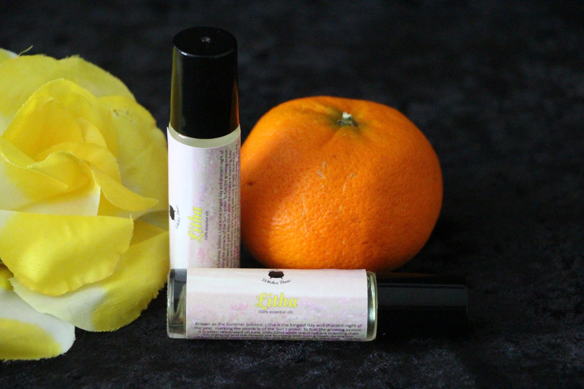 Litha essential oil roller bottles by Witches' Brew with orange and yellow rose on black fabric.