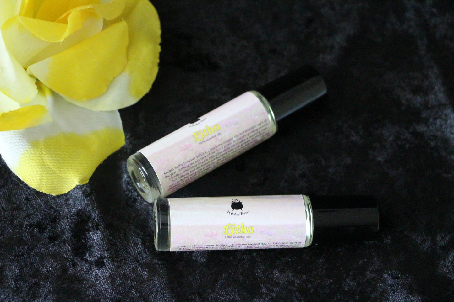 Two Witches' Brew Litha essential oil roller bottles on black velvet with yellow flower