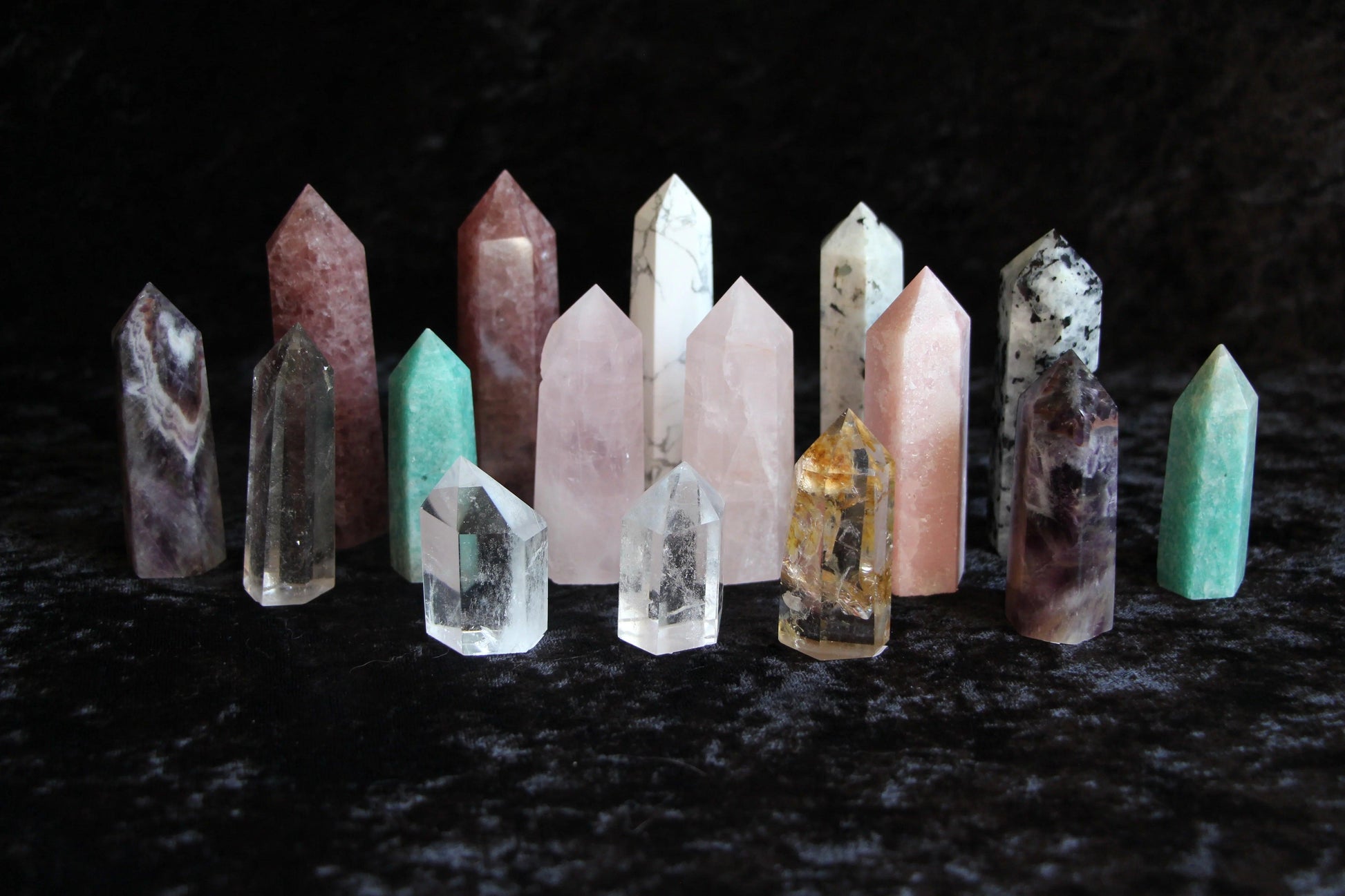 Collection of polished crystal point stones in various colors on black velvet background