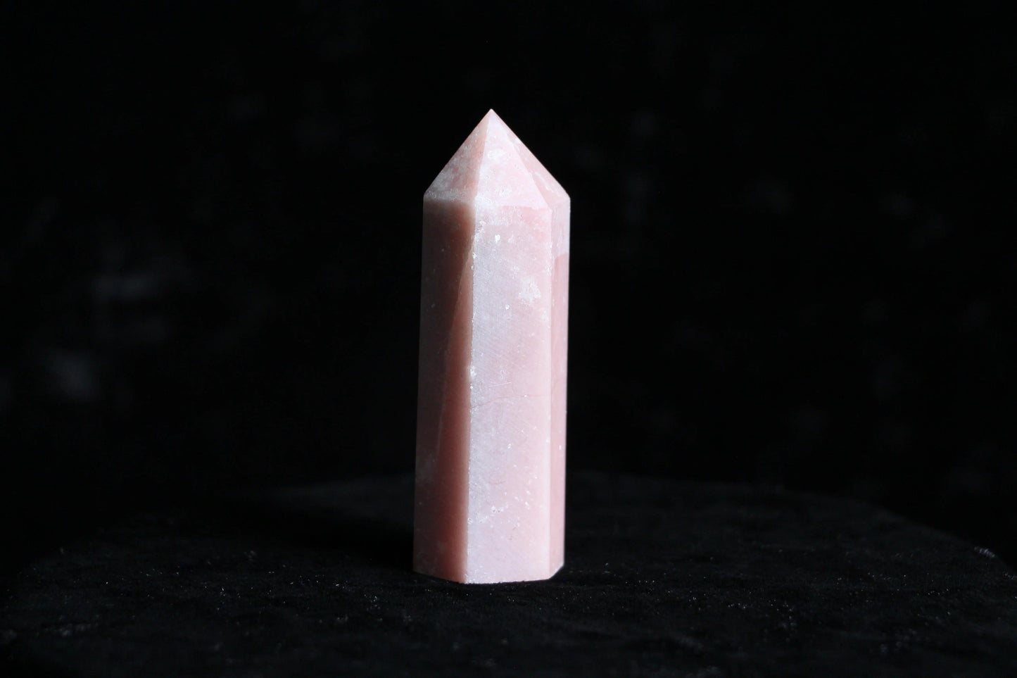 Pink polished rose quartz crystal point standing on black velvet background