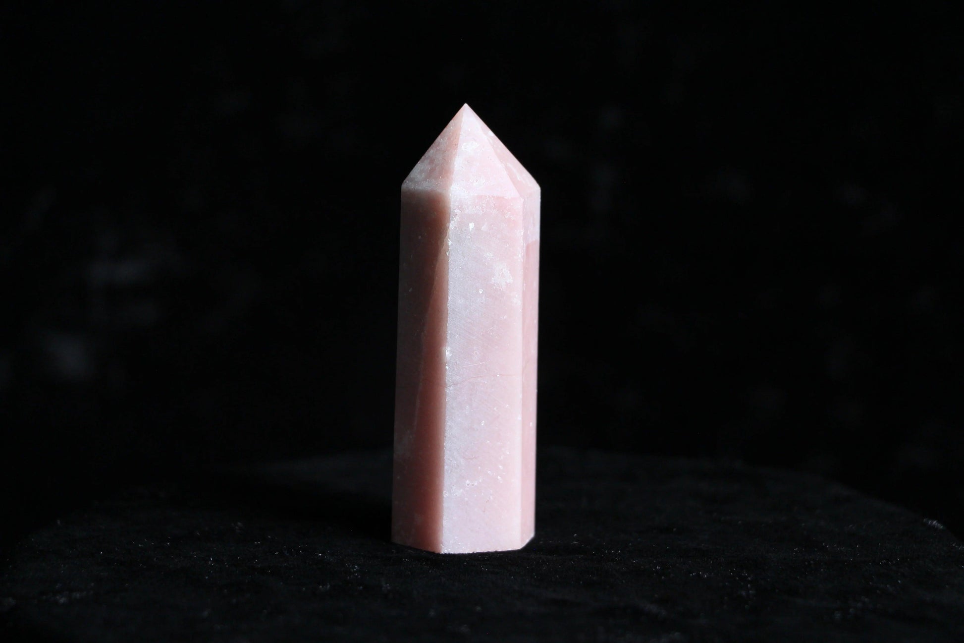Pink polished rose quartz crystal point standing on black velvet background