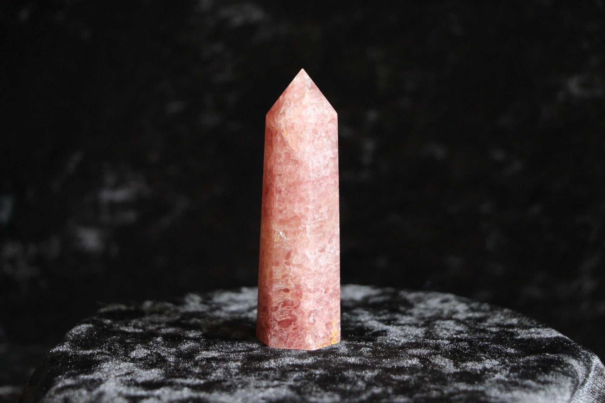 Polished rose quartz crystal point standing on textured black velvet surface with dark background