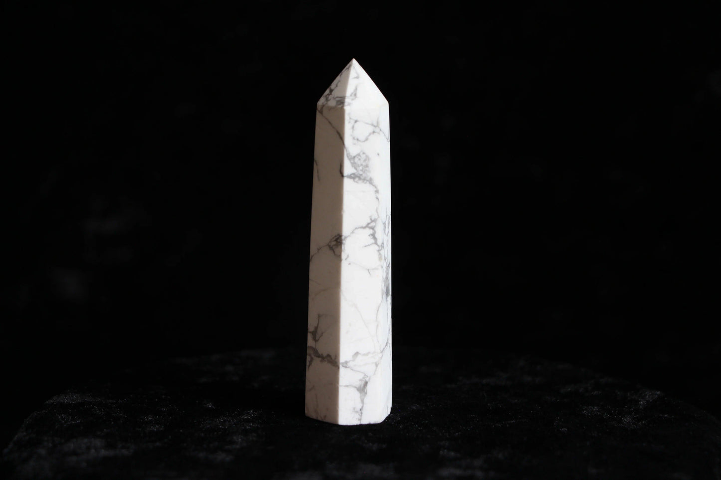 White marble quartz crystal tower with gray veining on black velvet background