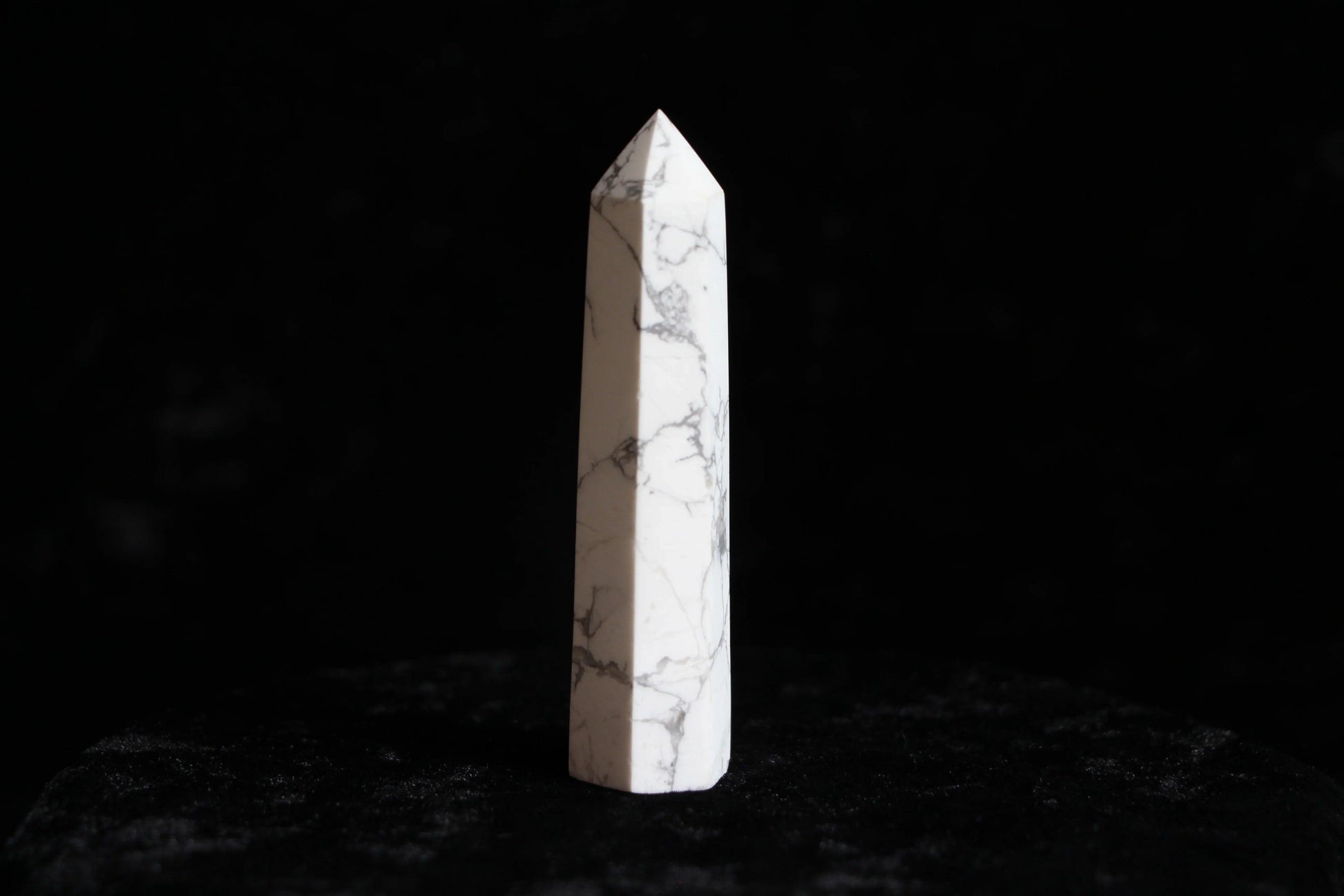 White marble quartz crystal tower with gray veining on black velvet background