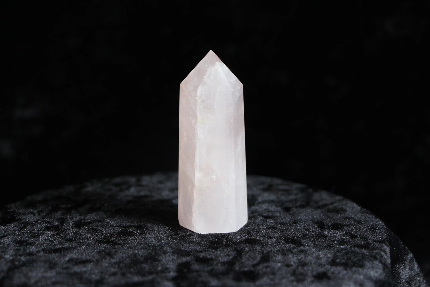 Polished rose quartz crystal point standing on textured black surface with dark background