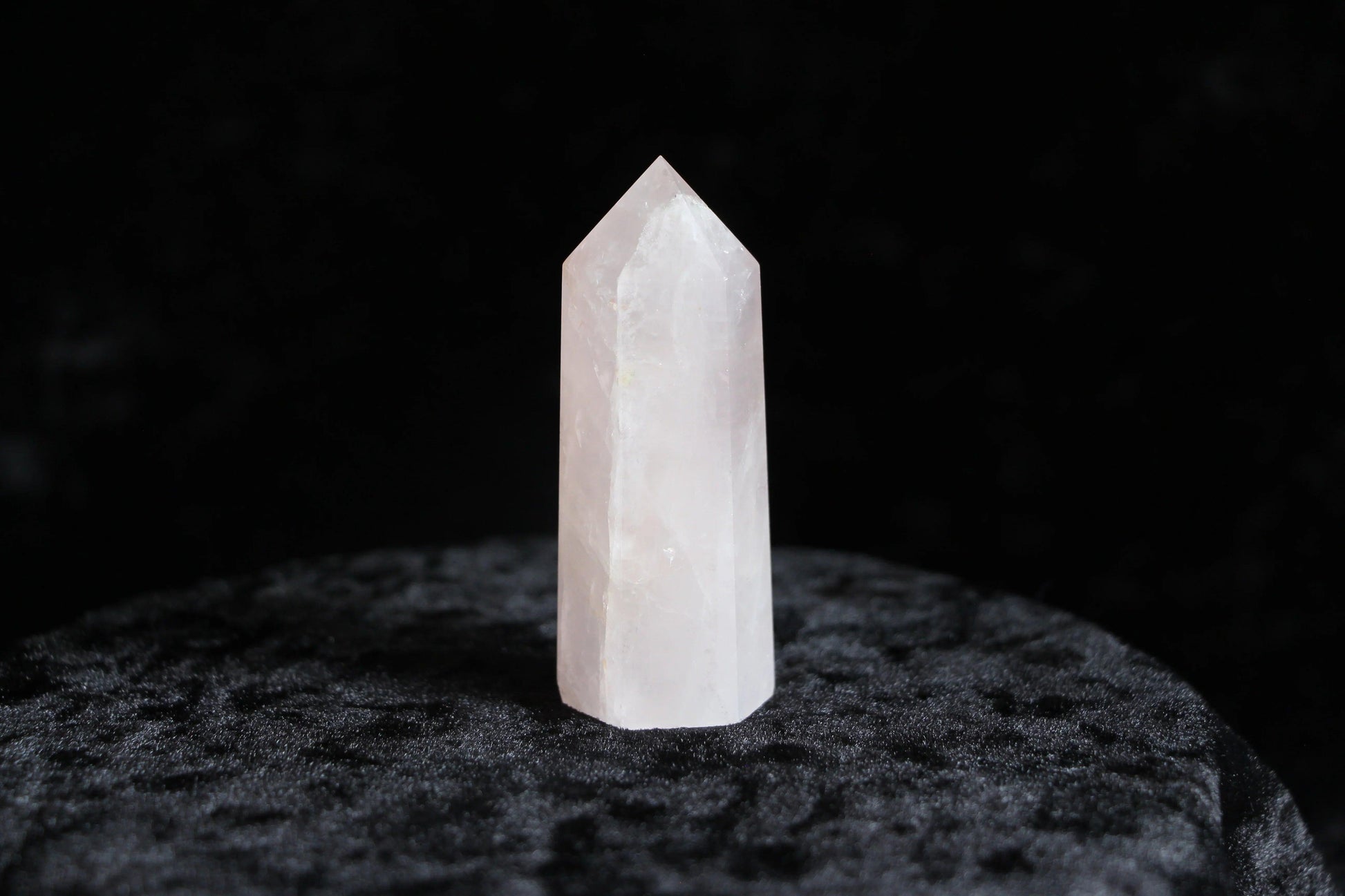 Polished rose quartz crystal point standing on textured black surface with dark background