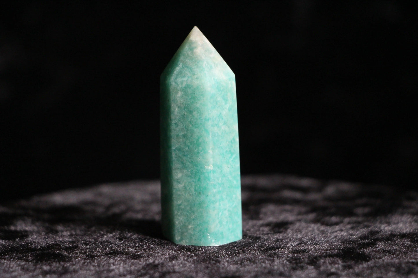 Polished green amazonite crystal standing upright on dark textured surface with black background