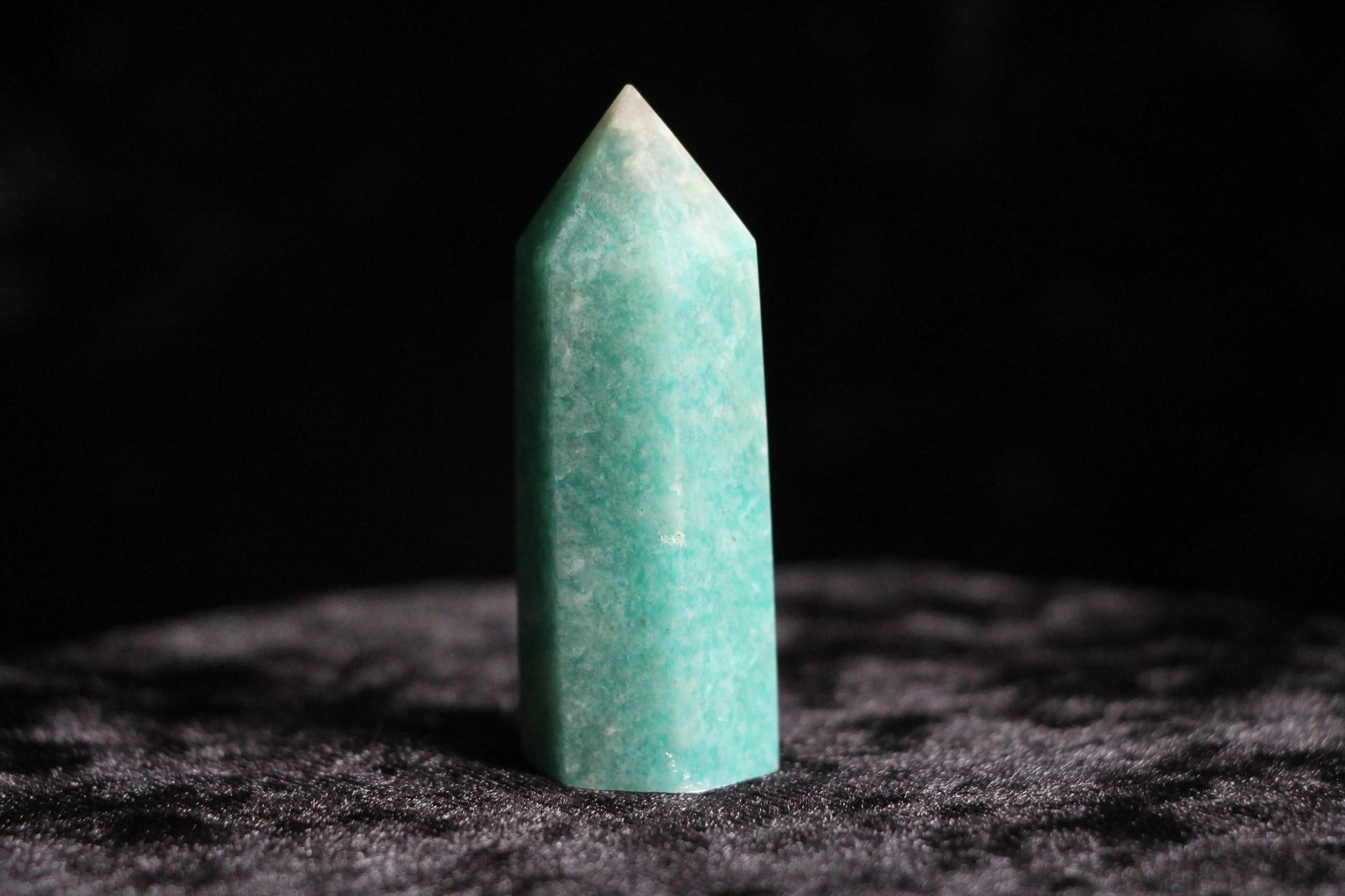 Polished green amazonite crystal standing upright on dark textured surface with black background