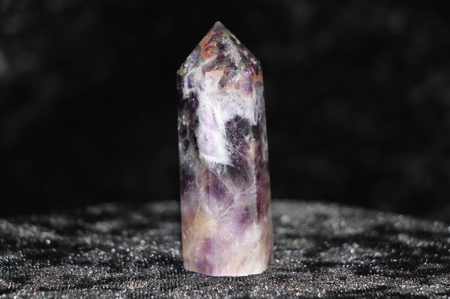 Polished amethyst crystal point with purple and white hues on black textured surface