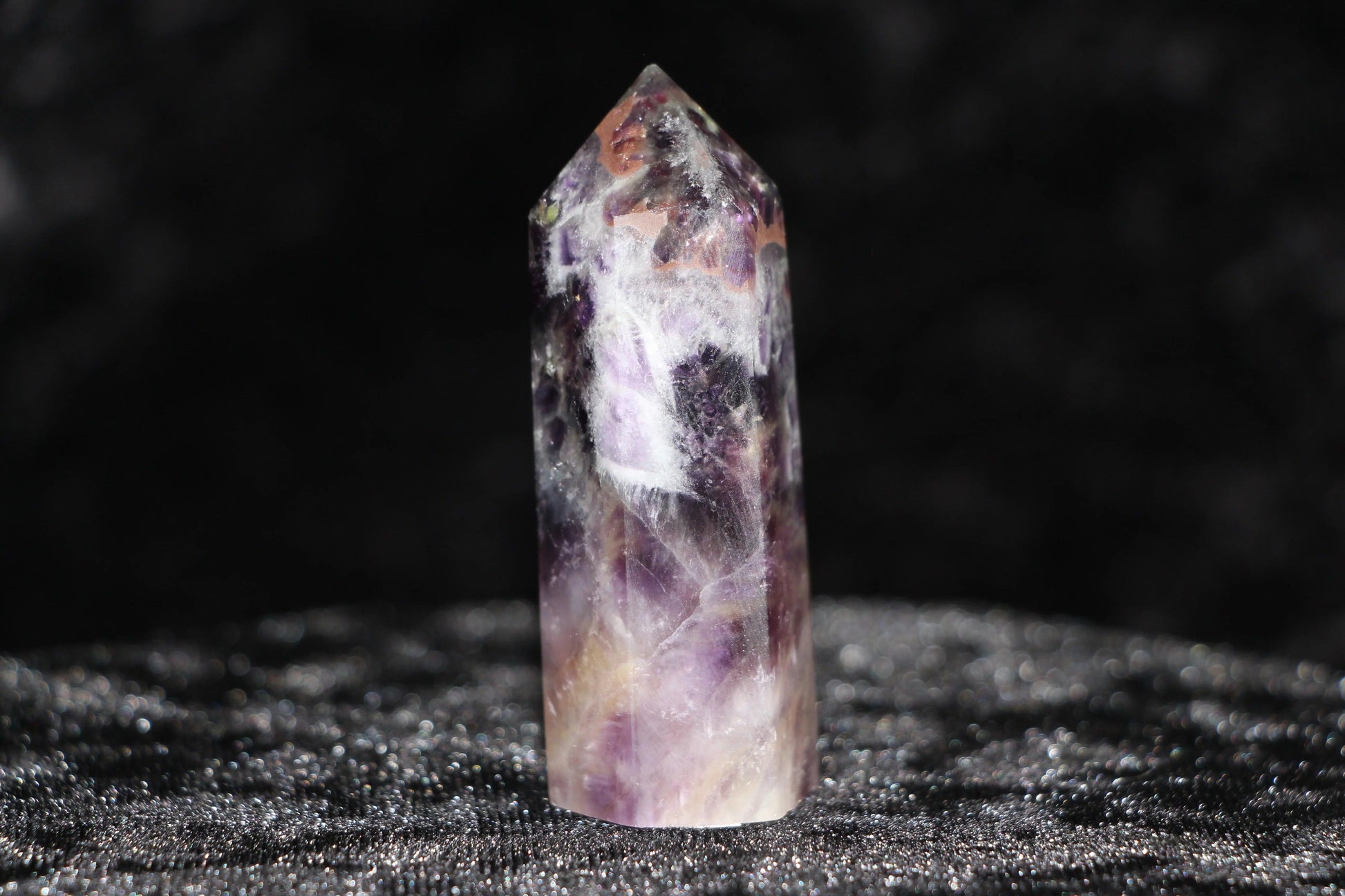 Polished amethyst crystal point with purple and white hues on black textured surface