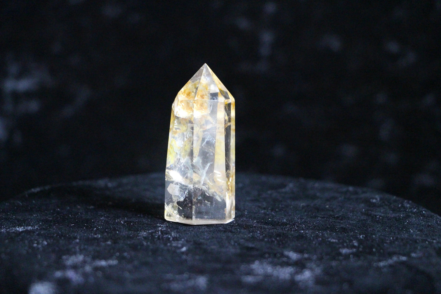 Clear yellow citrine crystal point standing on dark velvet surface against black background