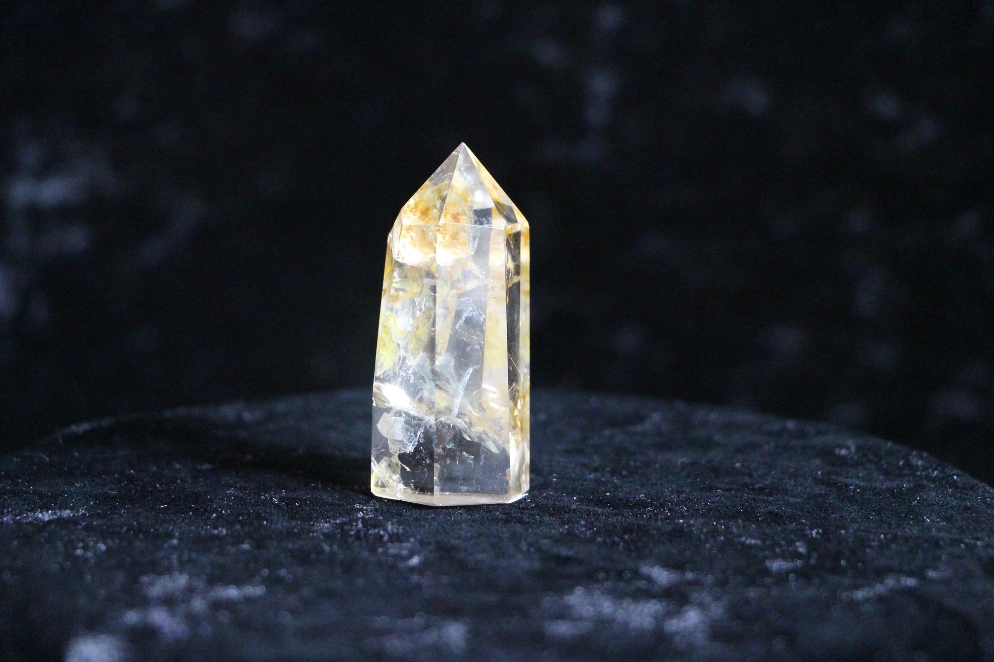 Clear yellow citrine crystal point standing on dark velvet surface against black background