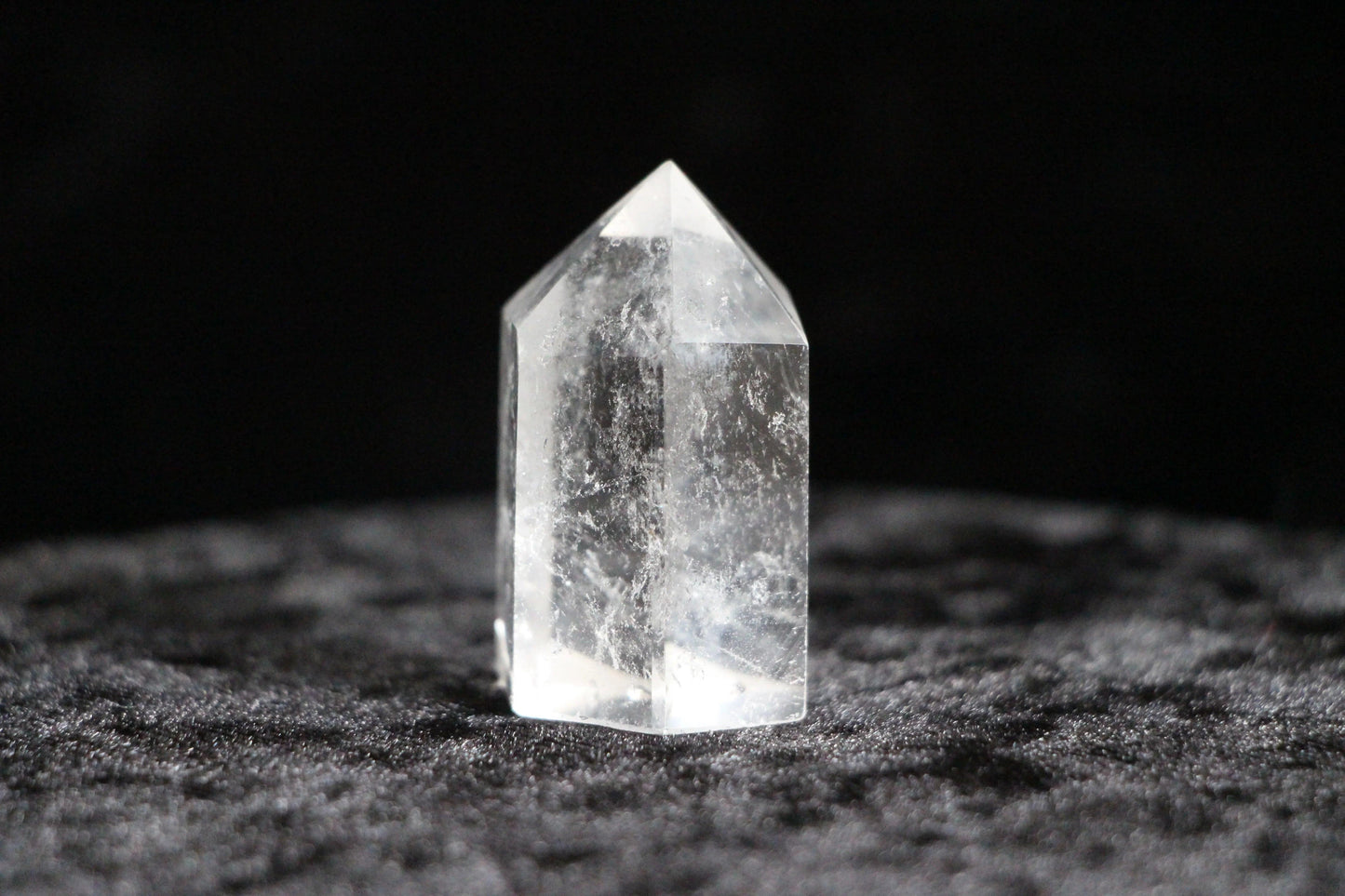 Clear quartz crystal point standing on textured black fabric background
