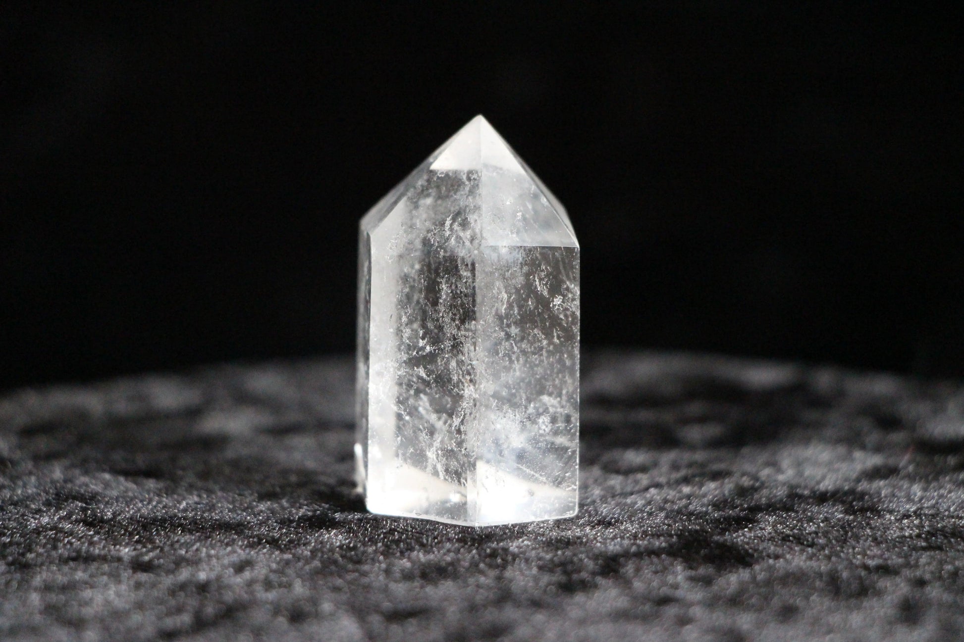 Clear quartz crystal point standing on textured black fabric background