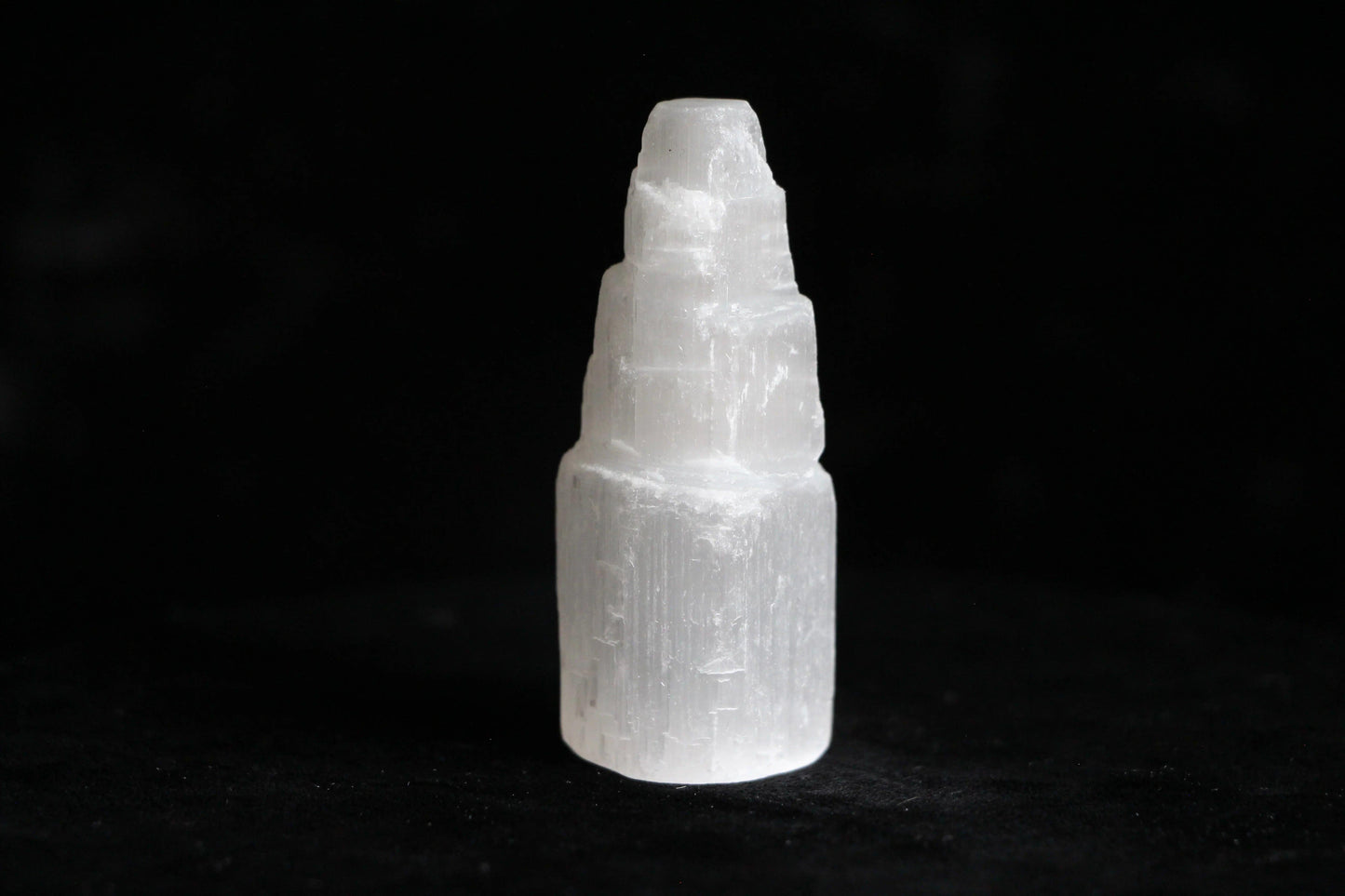 White selenite crystal tower on black surface with textured layers and polished edges