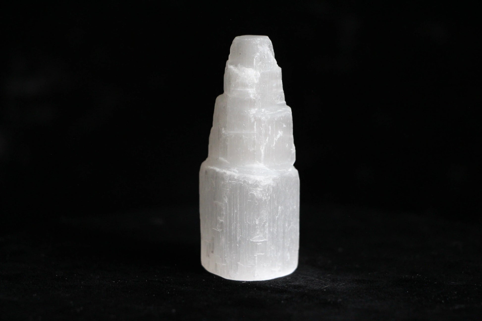 White selenite crystal tower on black surface with textured layers and polished edges