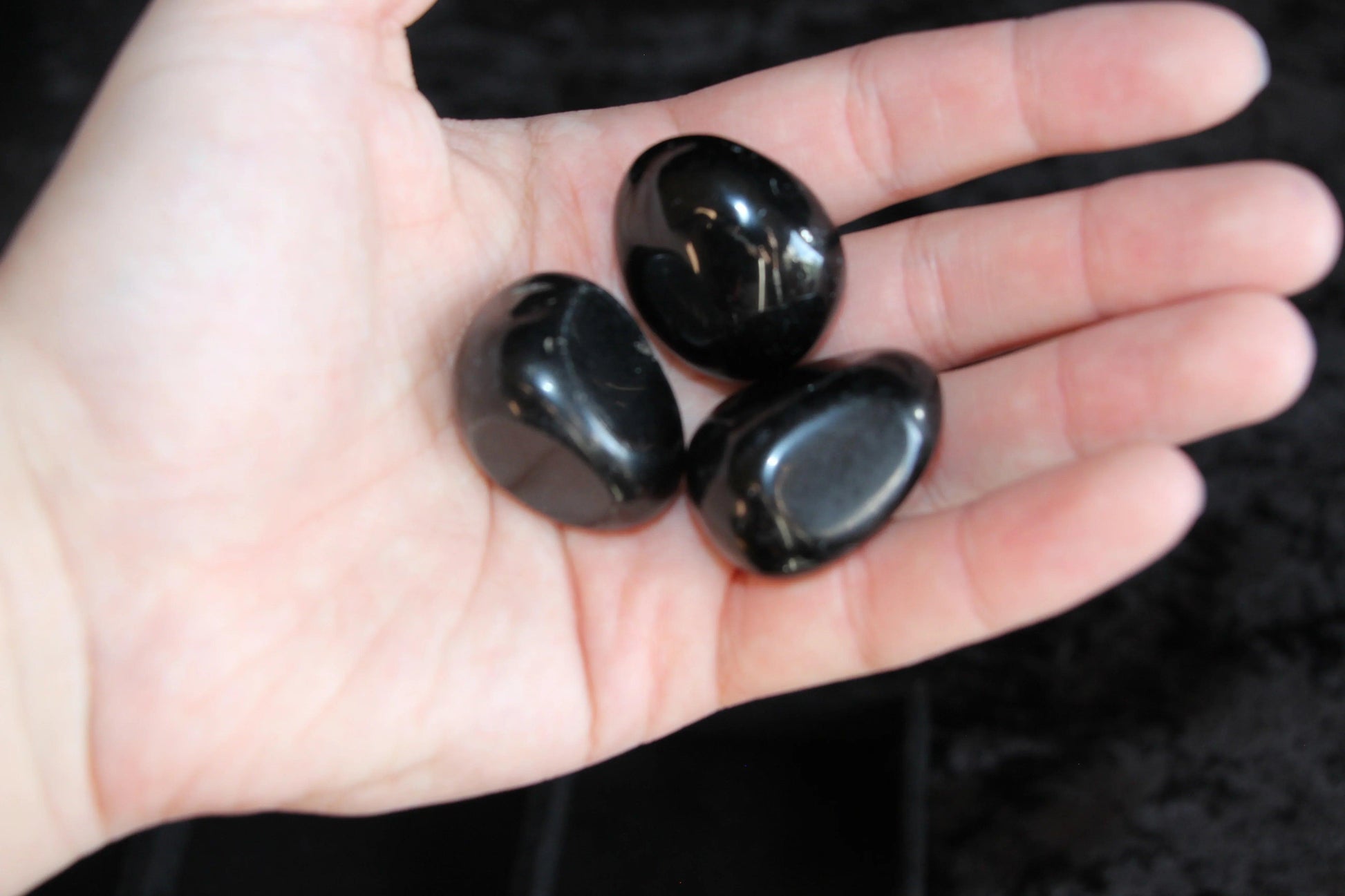 Hand holding three polished black stones, Witches' Brew ritual tool