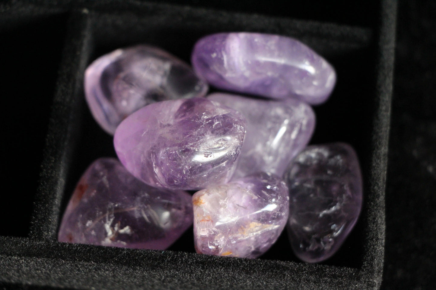 Close-up of polished amethyst stones in a black velvet jewelry box compartment