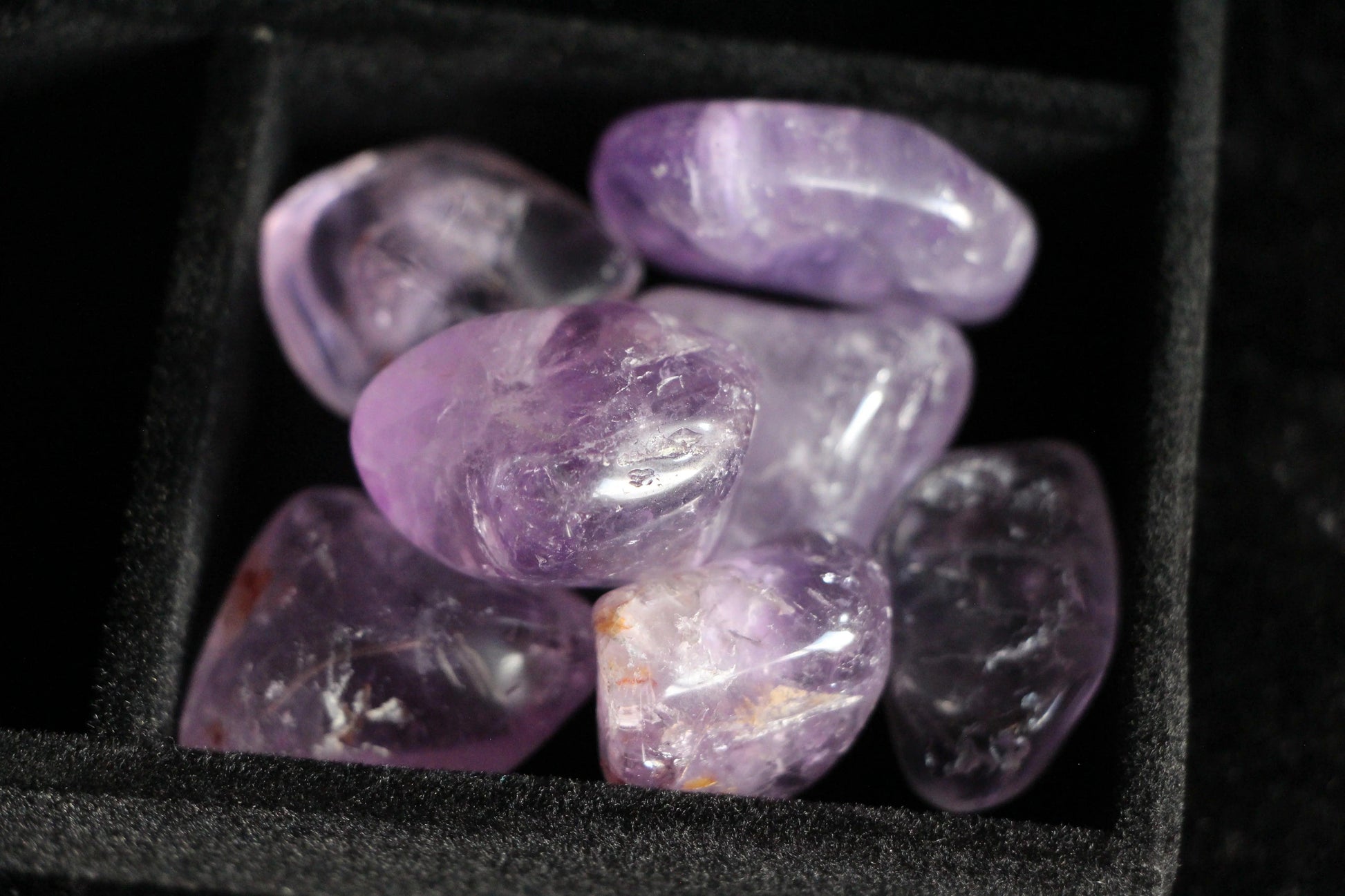 Close-up of polished amethyst stones in a black velvet jewelry box compartment