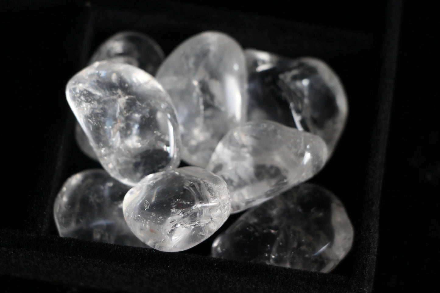 Clear quartz crystal tumble stones in a black tray, sustainable witchcraft supplies