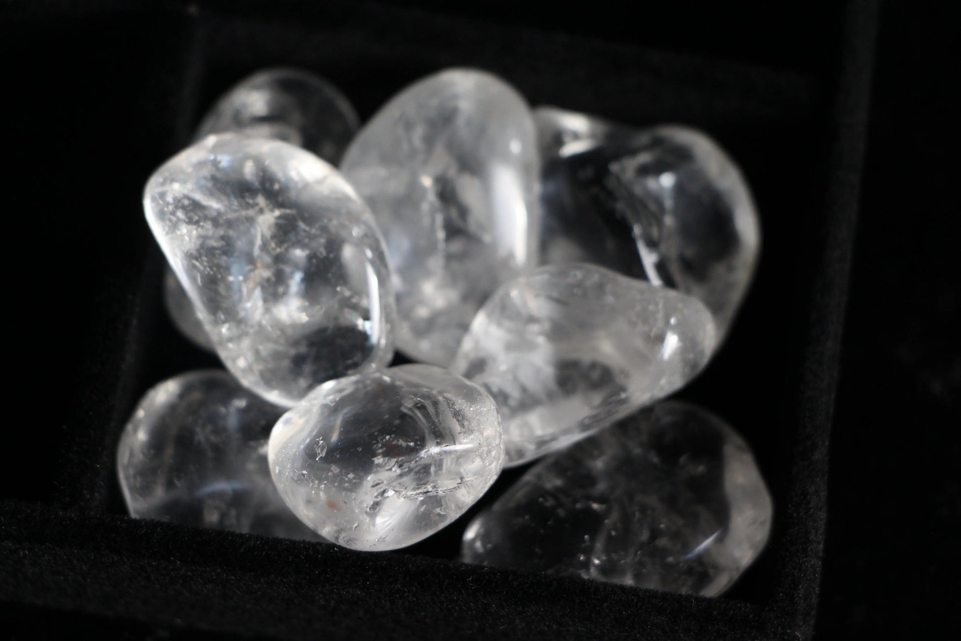 Clear quartz crystal tumble stones in a black tray, sustainable witchcraft supplies