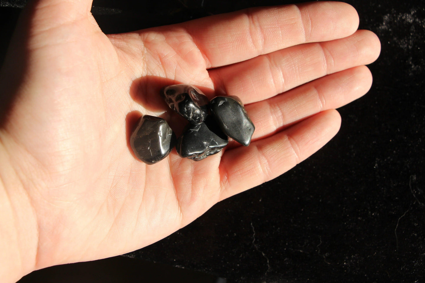 Hand holding four polished black crystals, ritual tool for modern witches